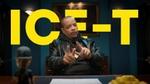 Persoon die aan een bureau zit en met beide handen gebaart, met grote gele tekst "ICE-T" op de achtergrond.