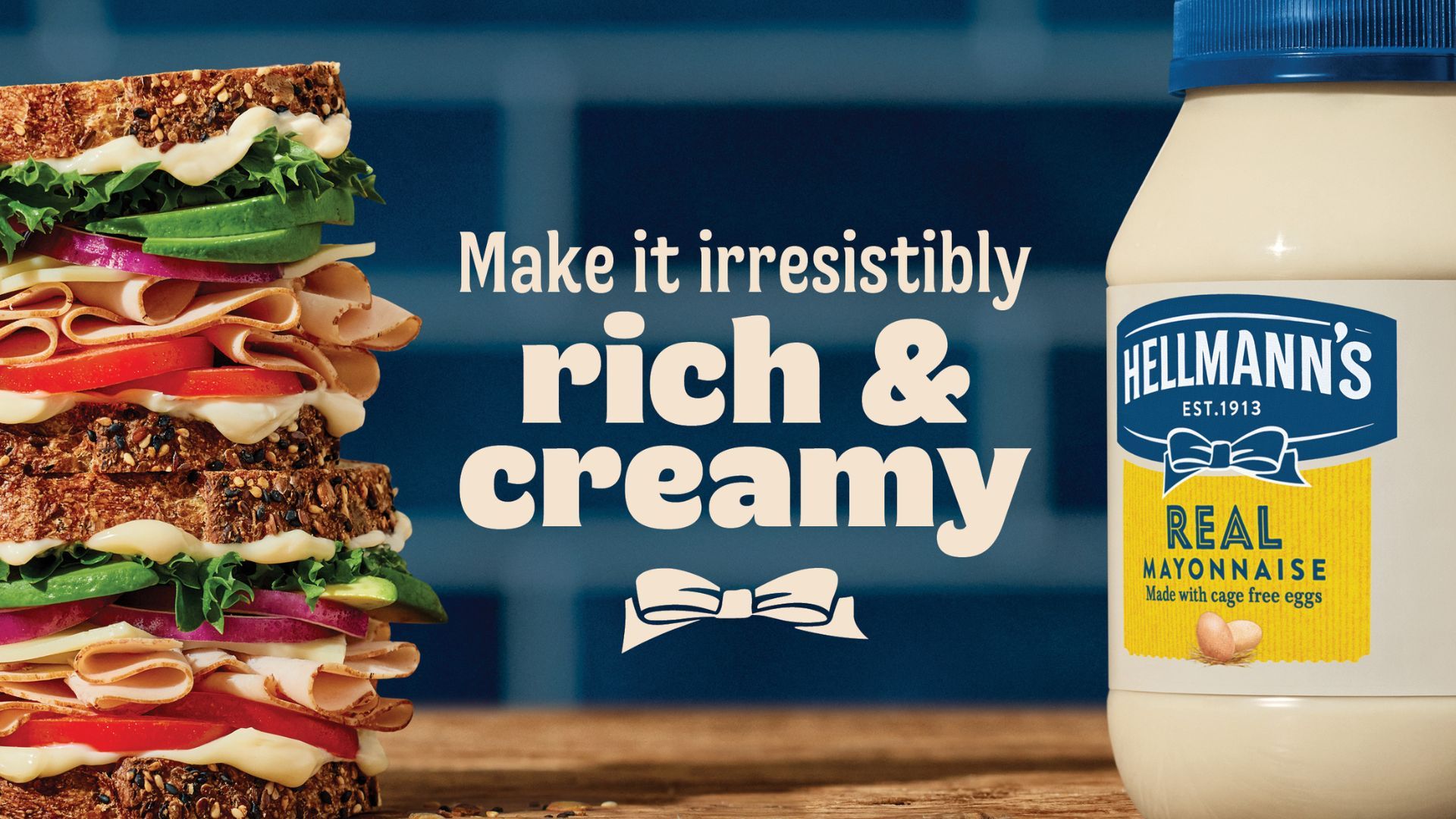 Op de banner staat een grote sandwich belegd met tomaat, kipfilet, komkommer, uit en sla. rechts daarvan een grote pot Hellman's mayonaise. in het midden staat de quote “make it irresistibly. rich & creamy”